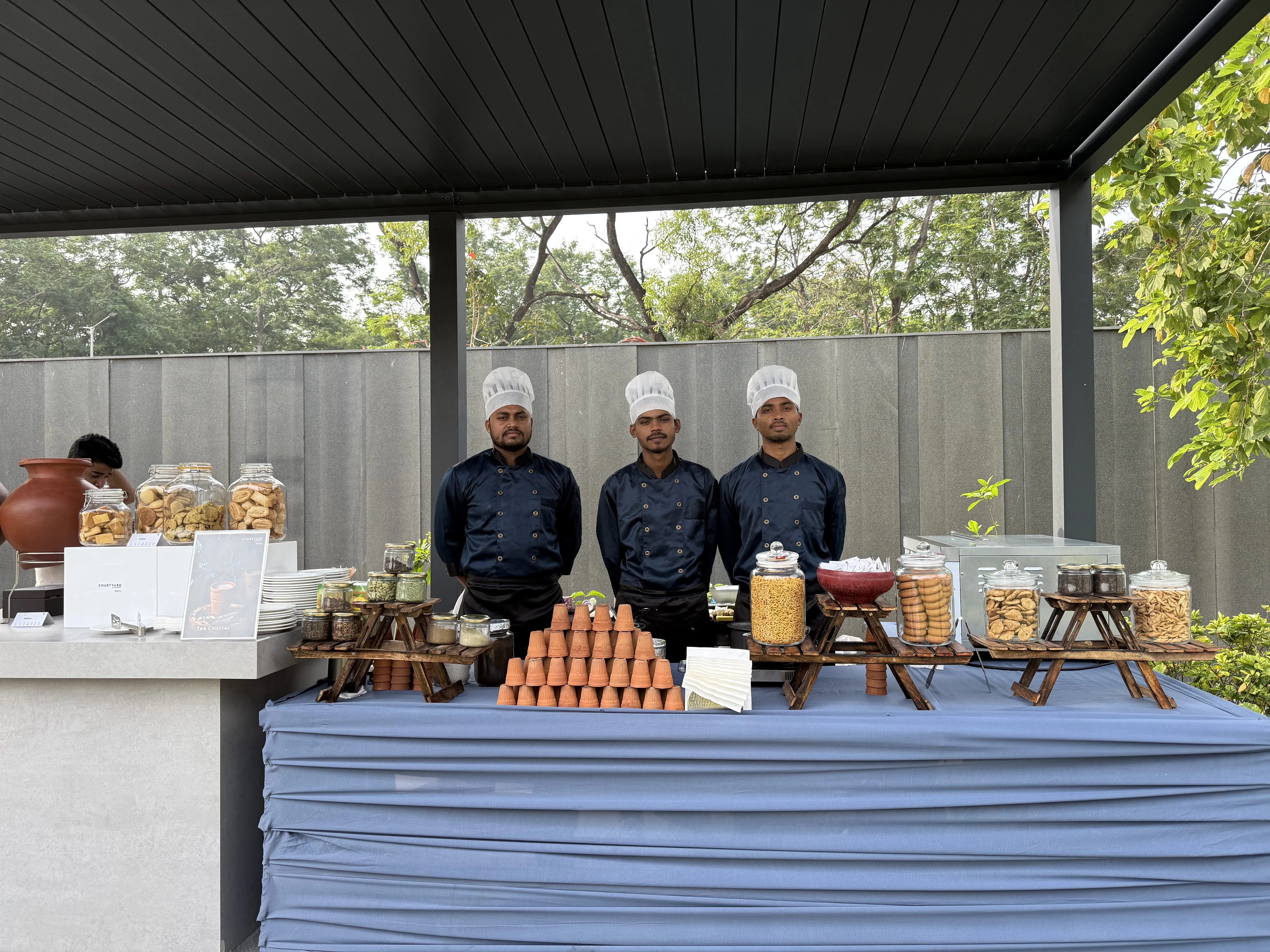 Chefs behind a live chai counter - kulhads stacked, clay matka, jars of biscuits